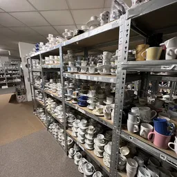 Metalen stellingen volgestapeld met wit servies, kopjes, kannen en ander keramiek
