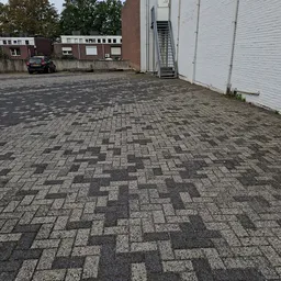 Parkeerterrein met kasseienpatroon naast witte garagedeur en bakstenen gebouw