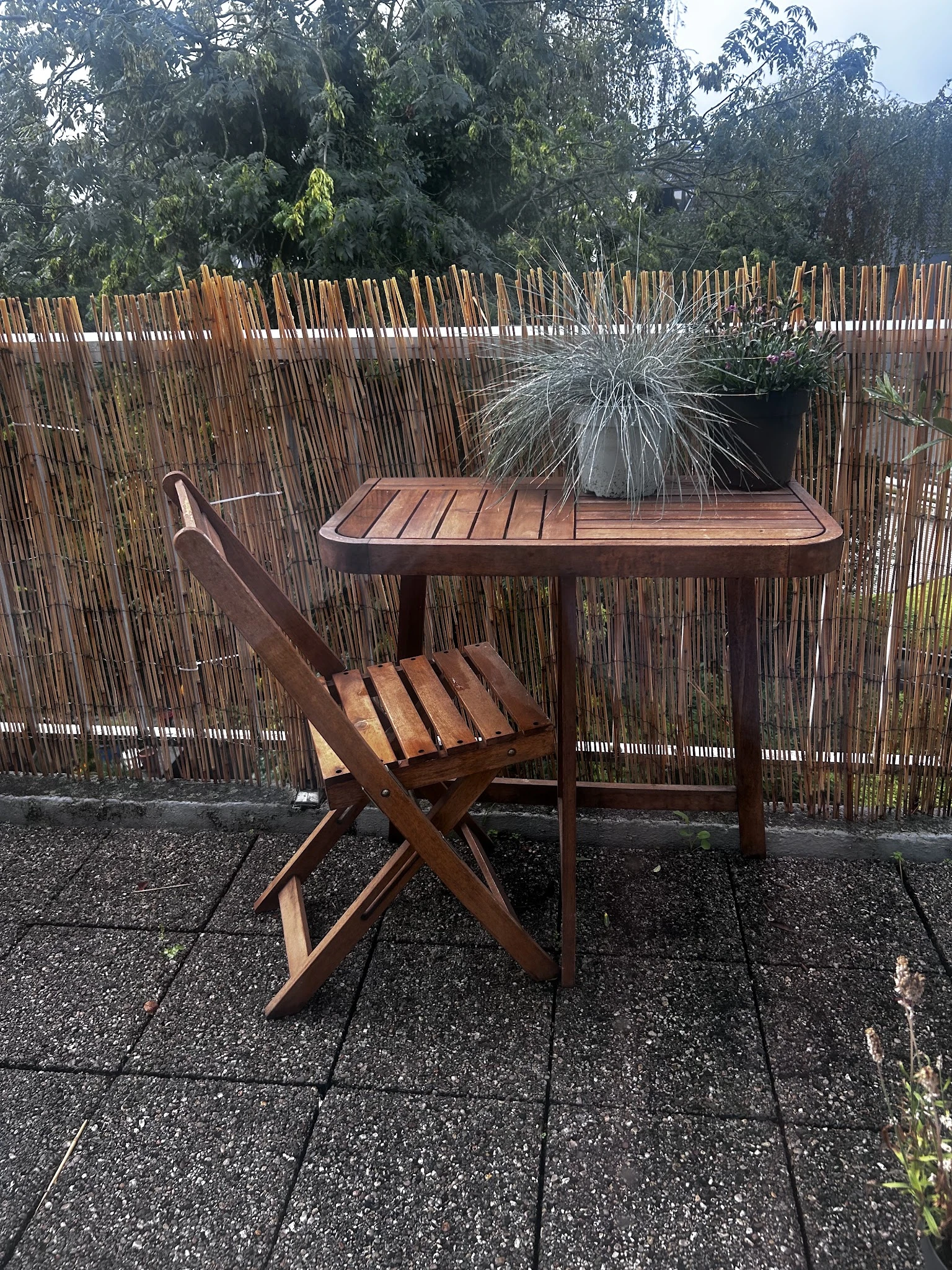 Houten eettafel met bijpassende stoel en plantenpot op een binnenplaats met houten schermen