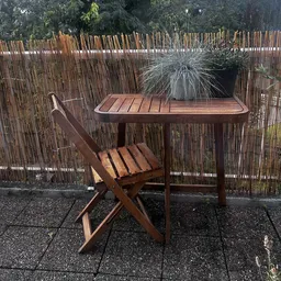 Houten eettafel met bijpassende stoel en plantenpot op een binnenplaats met houten schermen