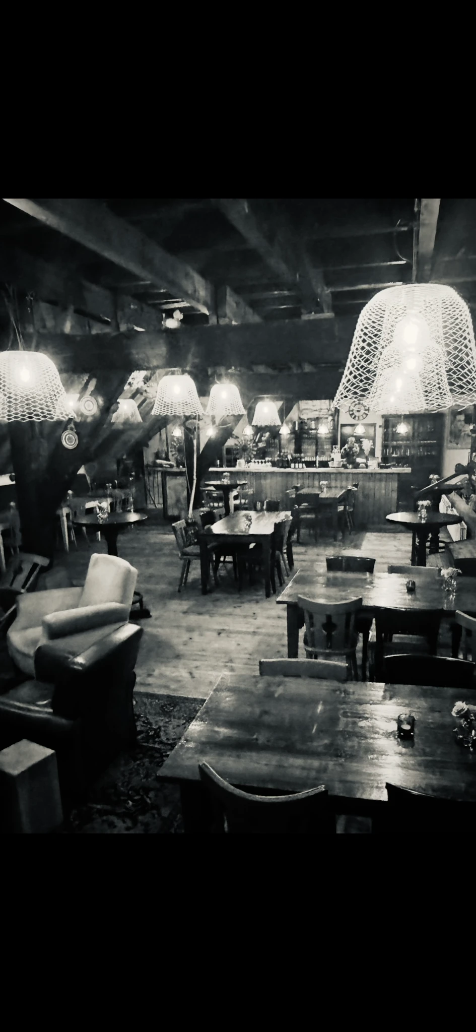 Zwart-witfoto van een lunchroom of cafetaria met tafels, stoelen en hangende lampen
