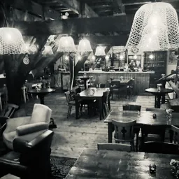 Zwart-witfoto van een lunchroom of cafetaria met tafels, stoelen en hangende lampen