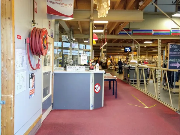 Winkelinterieur met balie, rode vloer, houten balken en stellingen met spullen in het achtergrondgedeelte.