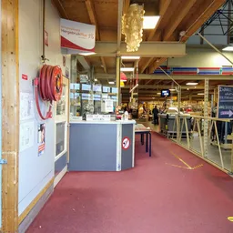 Binnenaanzicht van kringloopwinkel met balie, rode vloer, houten balken en stellingen met spullen