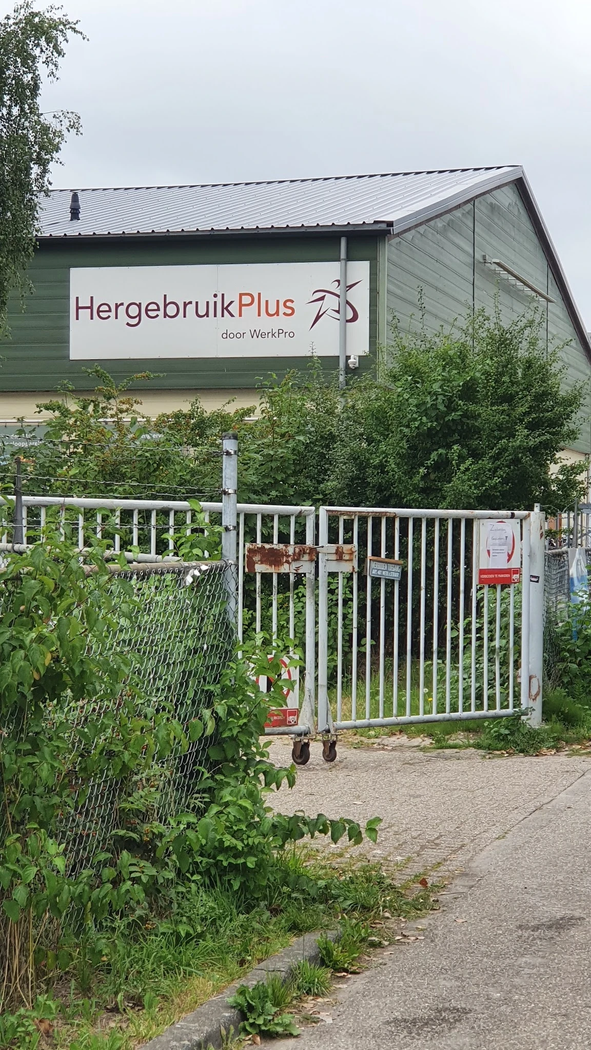 Witte toegangshek met bord 'HergebruikPlus door WerkPro' aan gevel van kringloopwinkel