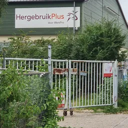 Witte toegangshek met bord 'HergebruikPlus door WerkPro' aan gevel van kringloopwinkel