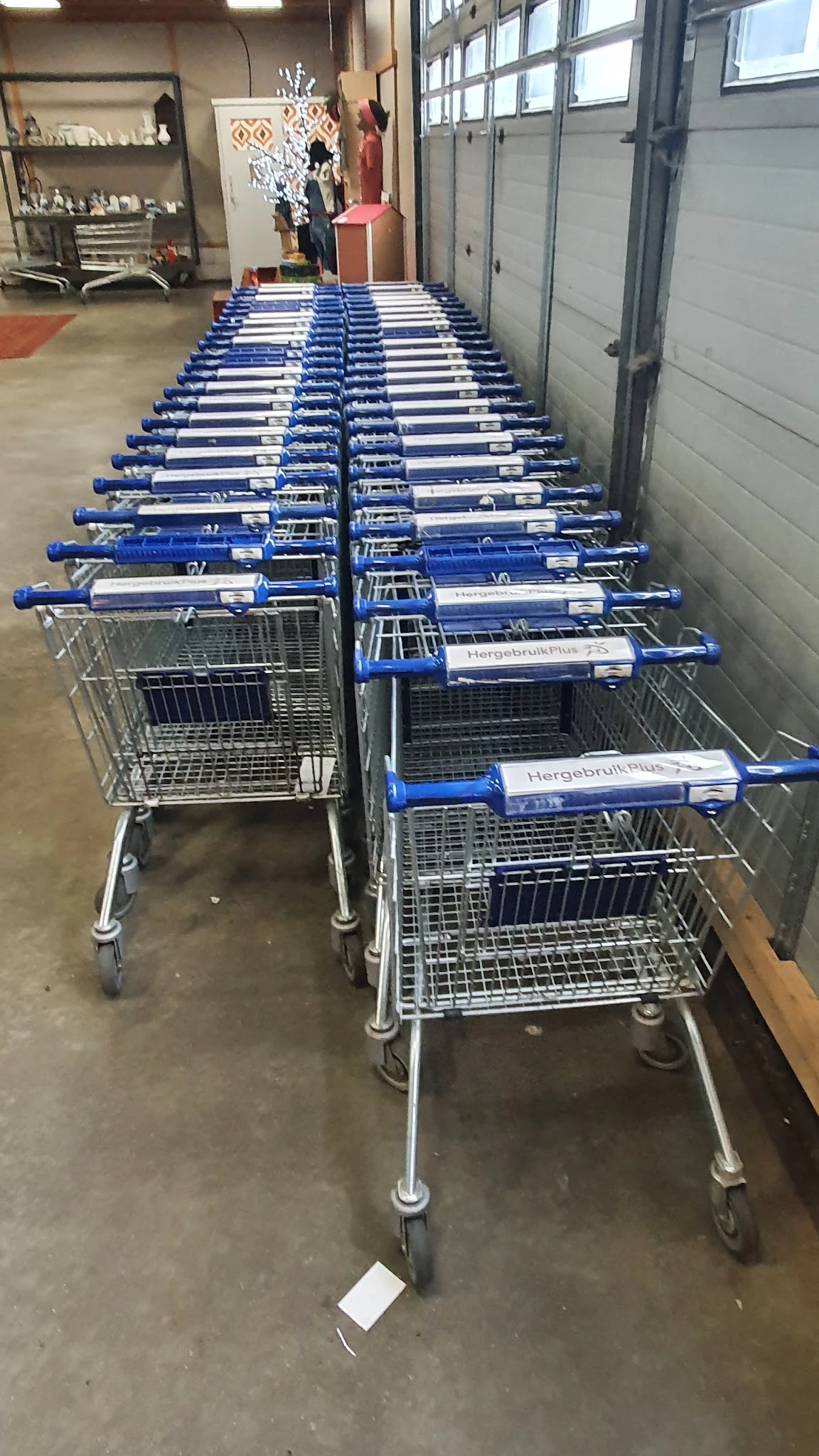 Rij van winkelwagens met blauwe mandje en naam Hergebruik Plus in kringloopwinkel