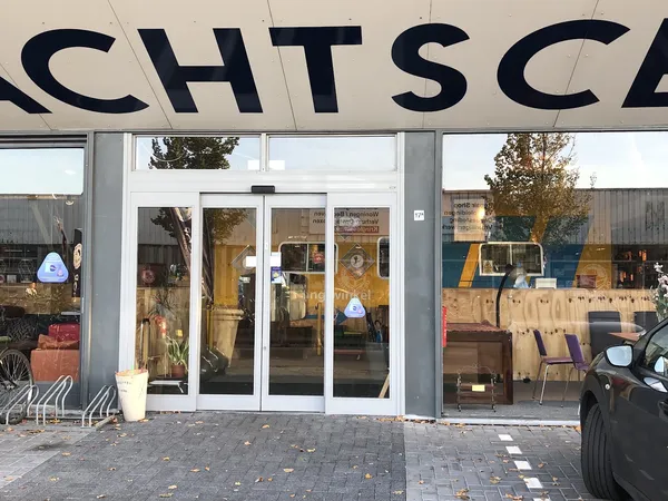 Winkelgevel met glasdeuren en grote zwarte letters van winkelnaam erboven, op een plein met voetgangerzone