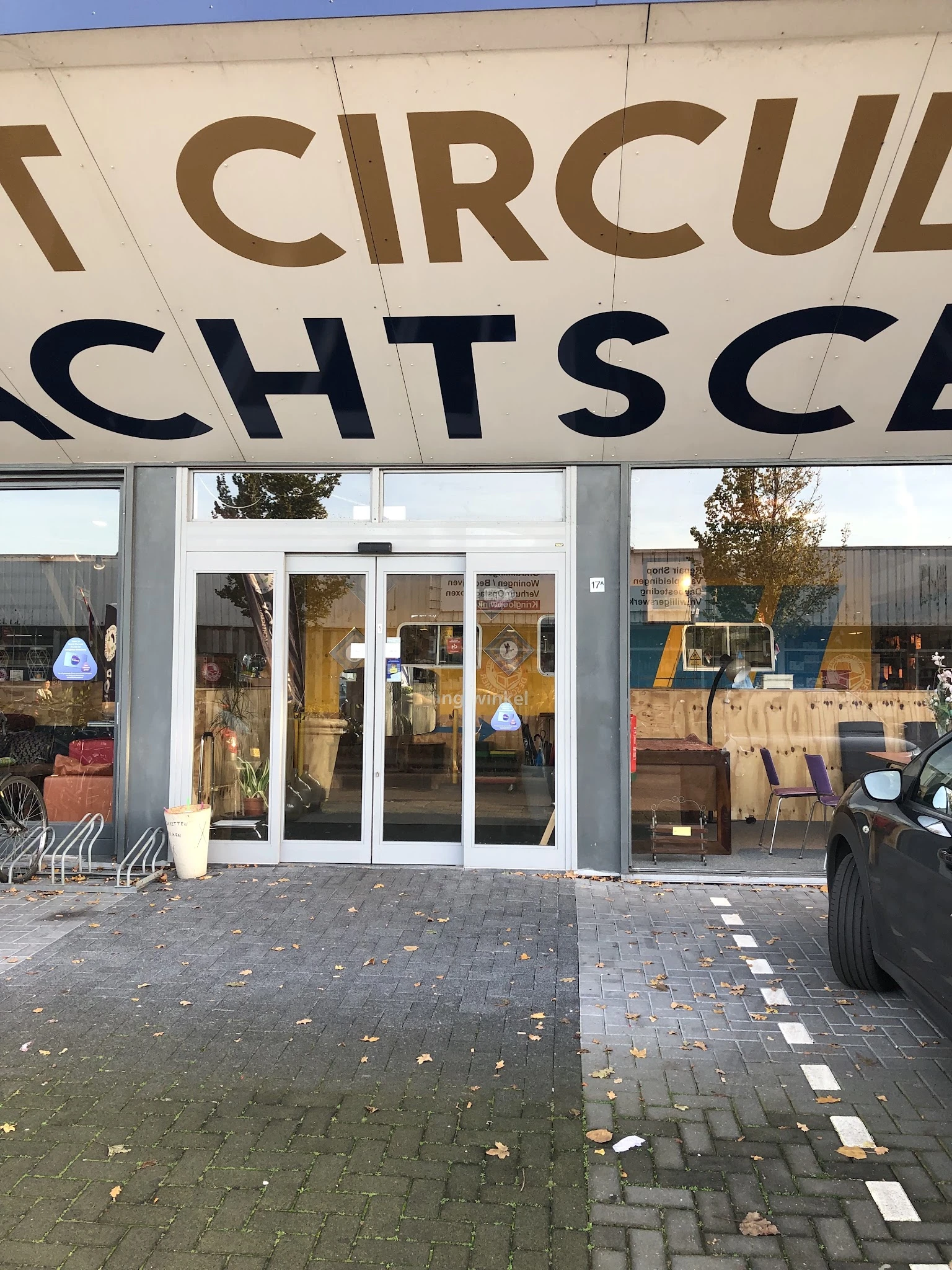 Winkelgevel met glasdeuren en grote zwarte letters van winkelnaam erboven, op een plein met voetgangerzone