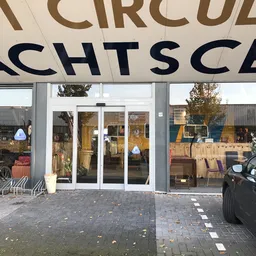 Winkelgevel met glasdeuren en grote zwarte letters van winkelnaam erboven, op een plein met voetgangerzone
