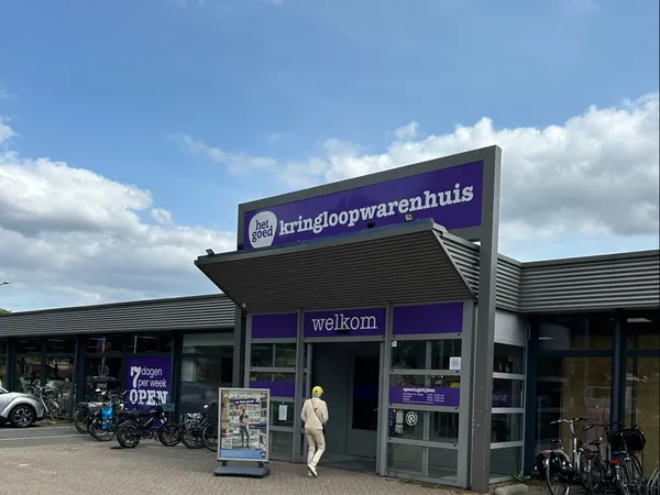 Voorgevel van kringloopwinkel met paarse belettering 'kringloopwarenhuis' en 'welkom', fietsen geparkeerd ervoor
