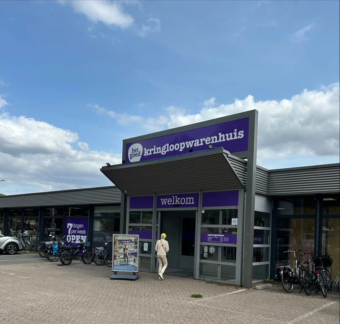 Voorgevel van kringloopwinkel met paarse belettering 'kringloopwarenhuis' en 'welkom', fietsen geparkeerd ervoor