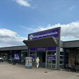 Voorgevel van kringloopwinkel met paarse belettering 'kringloopwarenhuis' en 'welkom', fietsen geparkeerd ervoor