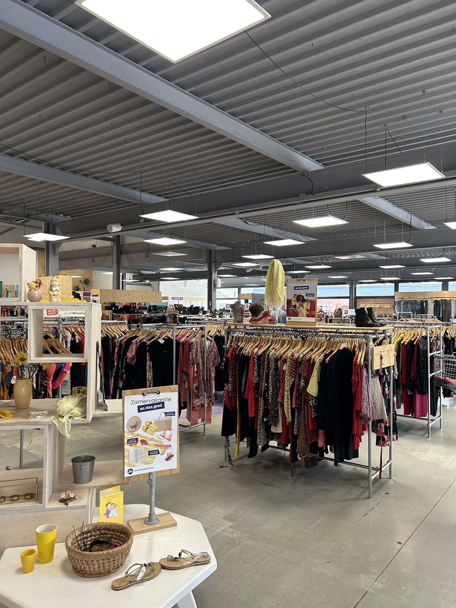 Kringloopwinkel met rekken vol tweedehands kleding in donkerrood en zwart, industrieel plafond met verlichting