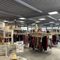 Kringloopwinkel met rekken vol tweedehands kleding in donkerrood en zwart, industrieel plafond met verlichting