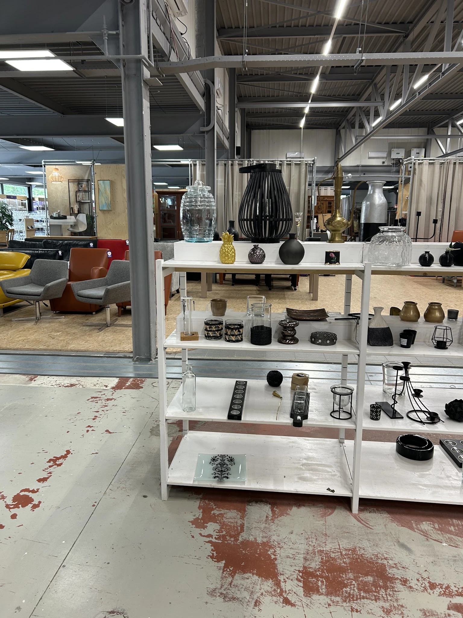 Witte stellingen met uitgestalde huishoudartikelen: vazen, schalen, kaarsenhouders en decoratieve items in zwart, beige en na