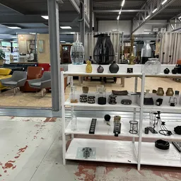 Witte stellingen met uitgestalde huishoudartikelen: vazen, schalen, kaarsenhouders en decoratieve items in zwart, beige en na