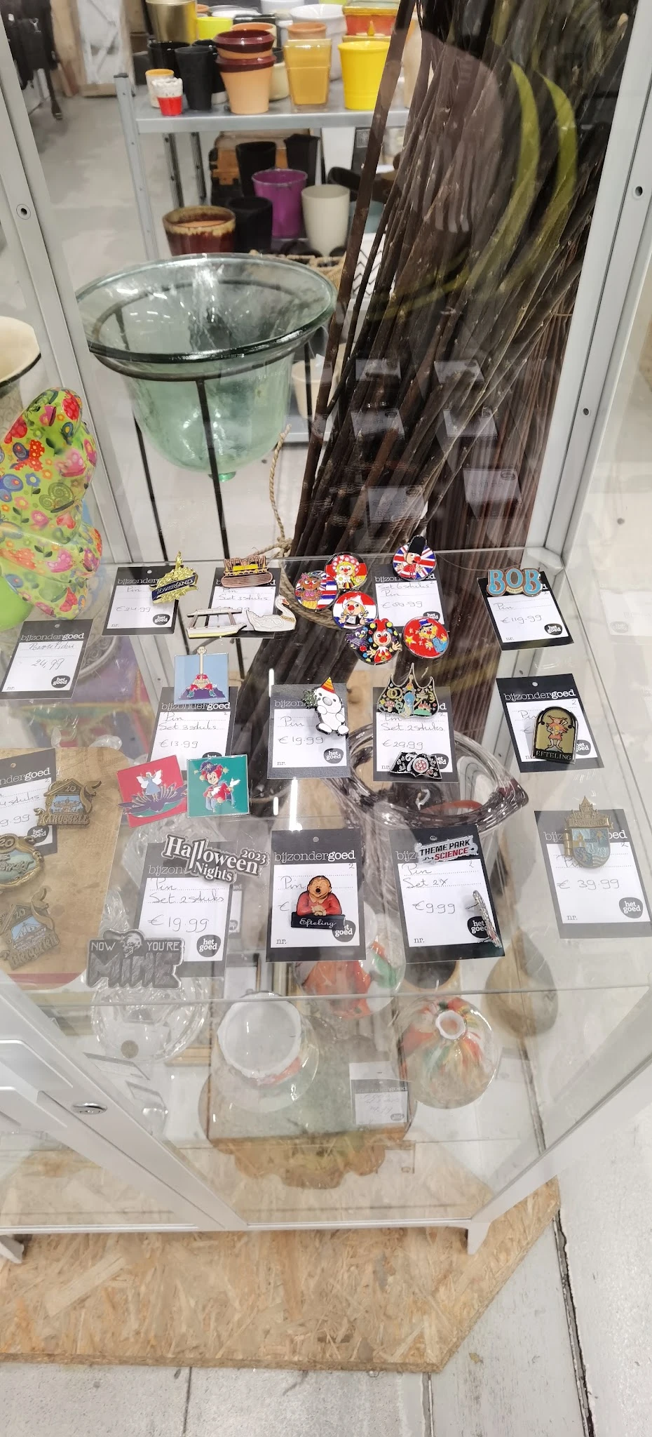 Uitgestalde verzameling souvenirs en merchandise items op glasplaten, waaronder sleutelhangers, pins en andere kleine gadgets