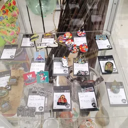 Uitgestalde verzameling souvenirs en merchandise items op glasplaten, waaronder sleutelhangers, pins en andere kleine gadgets