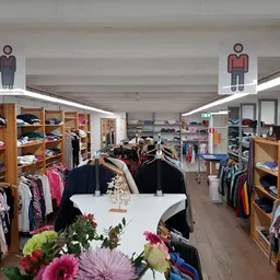 Winkelvloer van kringloopwinkel met houten stellingen vol kleding, bloemen op toonbank, mannelijk en vrouwelijk winkeltype-bo