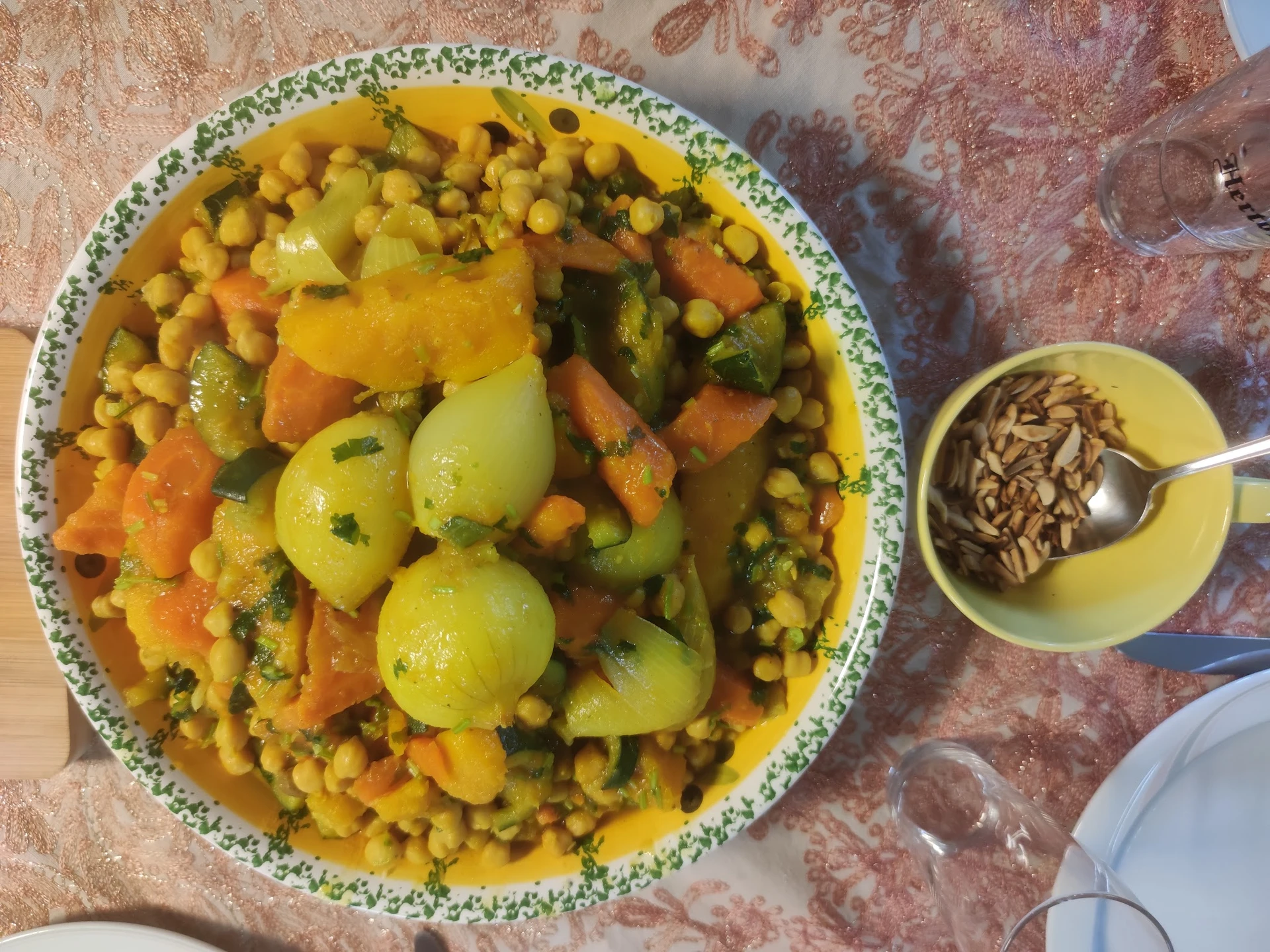 Bord met groenteschotel: mais, wortelen, aardappelen en erwten, met een bakje zaden ernaast