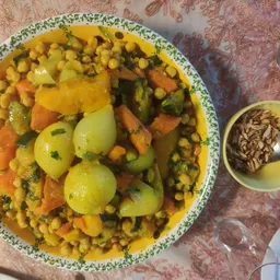 Bord met groenteschotel: mais, wortelen, aardappelen en erwten, met een bakje zaden ernaast
