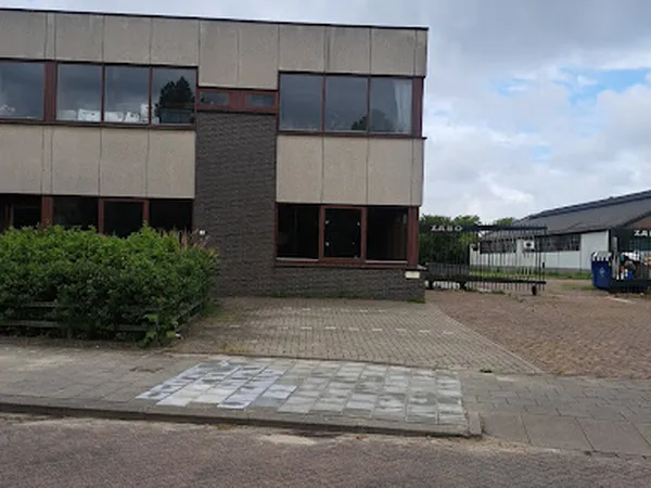 Voorgevel van moderne kringloopwinkel met bakstenen en beige panelen, pui op begane grond, inrit met tegels