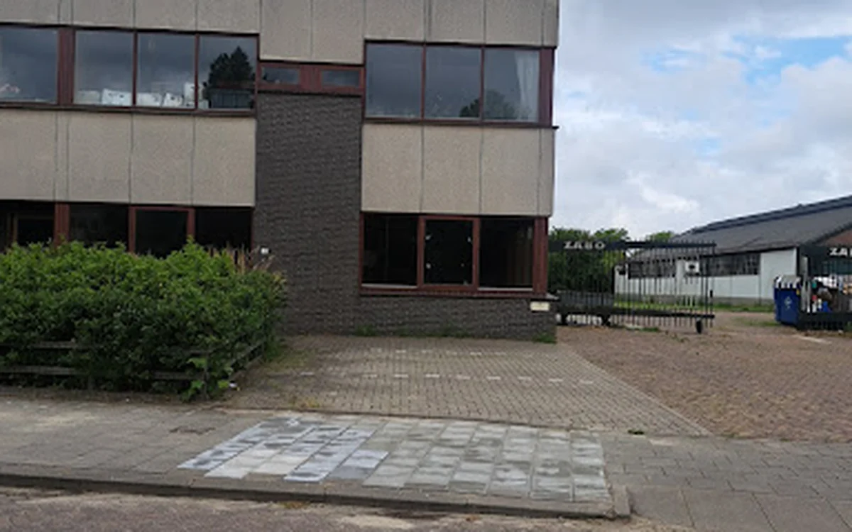 Voorgevel van moderne kringloopwinkel met bakstenen en beige panelen, pui op begane grond, inrit met tegels