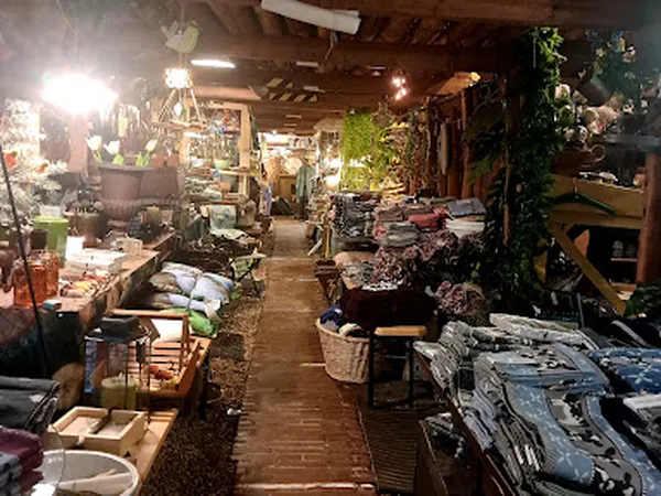 Brede winkelgang met rekken vol kleding en spullen, verlicht met hanglampen, groen klimop tegen rechtermuur