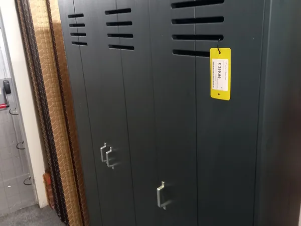 Zwarte kasten of servers met ventilatiesleuven en een geel etiket tegen een muur.