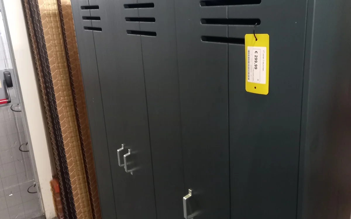 Zwarte kasten of servers met ventilatiesleuven en een geel etiket tegen een muur.