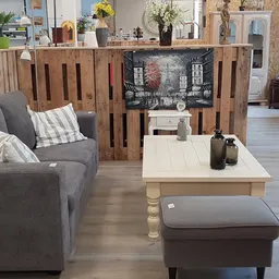 Woonkamerinrichting met grijze fauteuil, houten scheidingswand, witte salontafel en bruine poef in kringloopwinkel