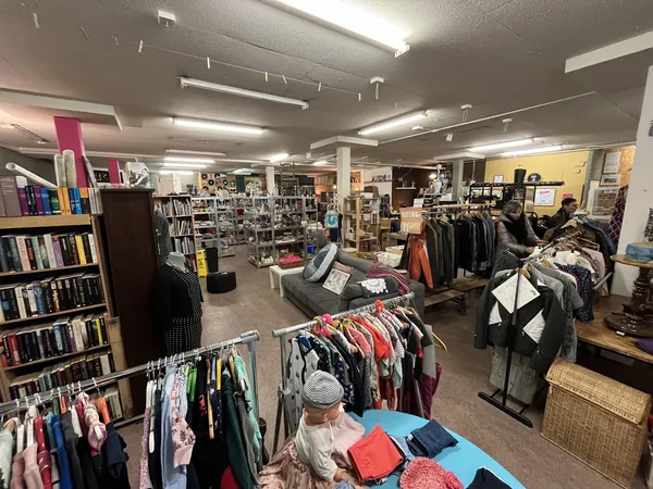 Overzicht van kringloopwinkelinterieur met kledingrekken, boekenkasten en diversen uitgestald