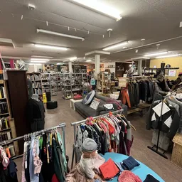 Winkelvloer van kringloopwinkel met kledingrekken, boekenkast en diversen spullen uitgestald