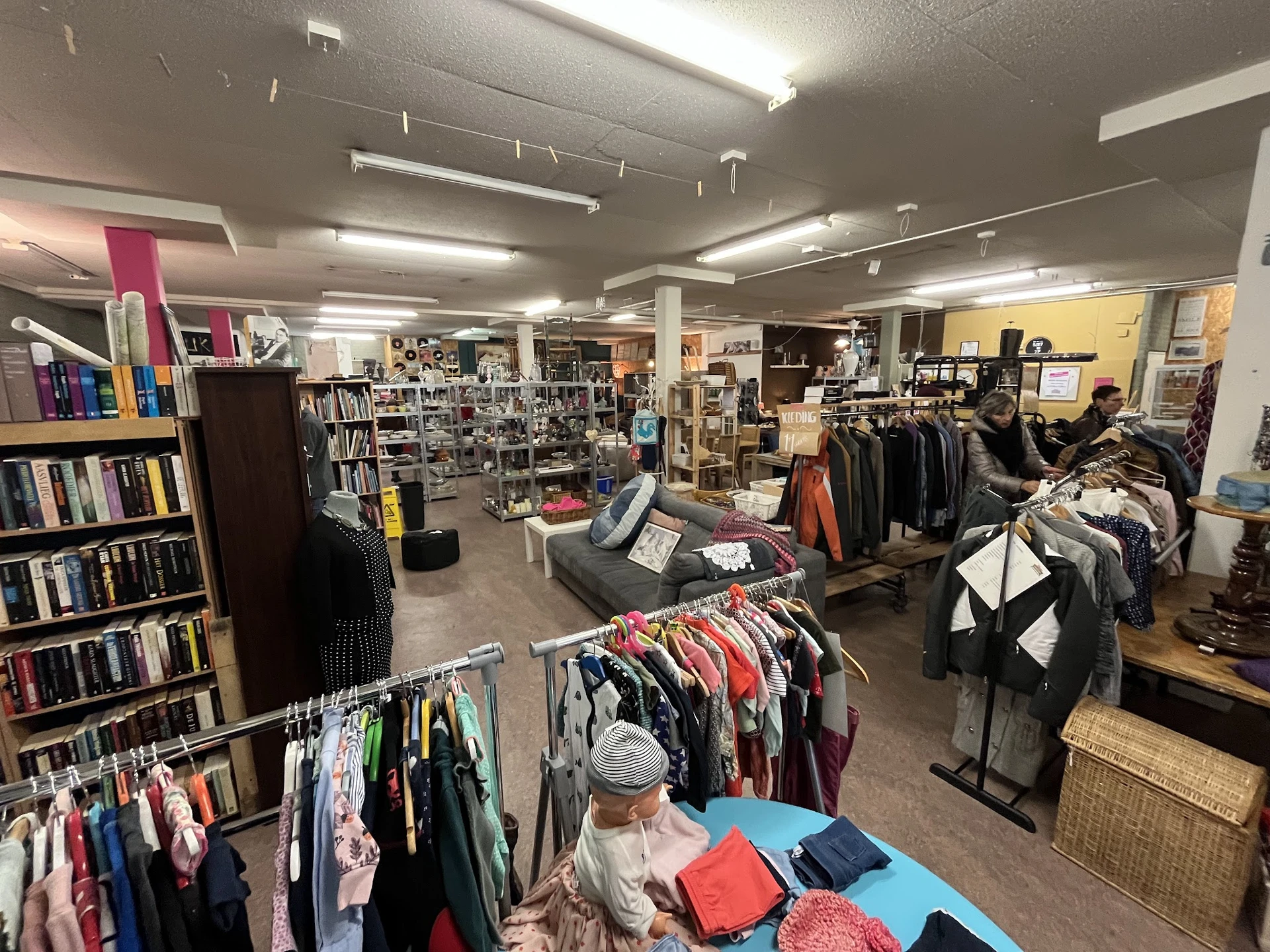 Winkelvloer van kringloopwinkel met rekken kleding, boekenkasten en diversen spullen uitgestald
