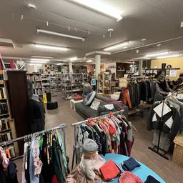 Winkelvloer van kringloopwinkel met rekken kleding, boekenkasten en diversen spullen uitgestald