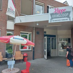 Ingang van Hippe Kringloop met terras, rode parasol, stoelen en oranje poefjes