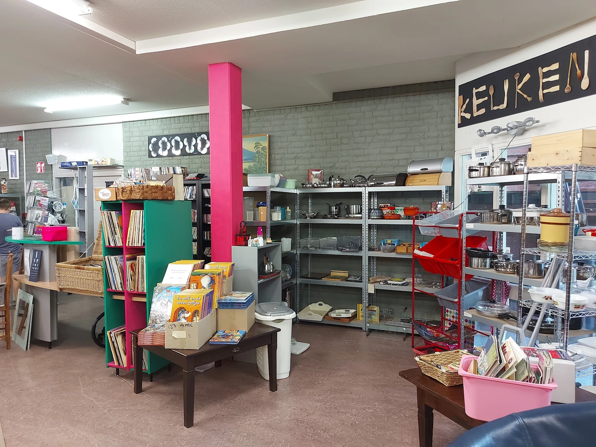 Winkelvloer met stellingen, boeken, speelgoed en diverse tweedehands artikelen; roze paal in het midden