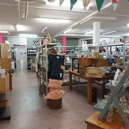 Ruime winkelvloer van kringloopwinkel met meubels, dozen en spullen verspreid uitgestald onder fluorescente verlichting