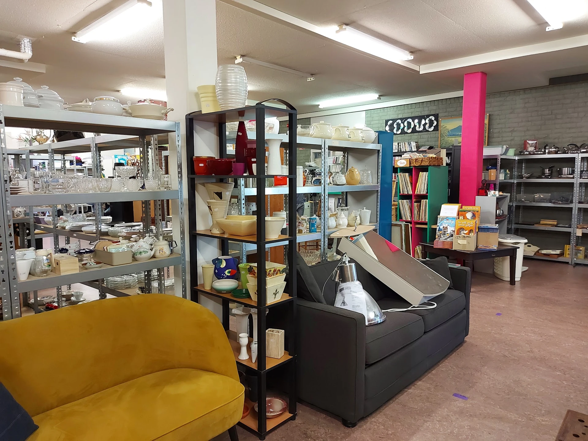 Winkelvloer met gele fauteuil, zwarte bank, kasten, boekenrekken en diverse tweedehands artikelen