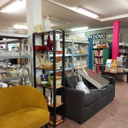 Winkelvloer met gele fauteuil, zwarte bank, kasten, boekenrekken en diverse tweedehands artikelen