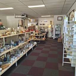 Binnenaanzicht van kringloopwinkel met tafels vol serviesgoed, vitrinekasten en diverse spullen langs de wanden