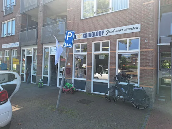 Voorgevel van kringloopwinkel met winkelnaam Kringloop erop, grote ramen, parkeerplaats met fietsen en auto's ervoor