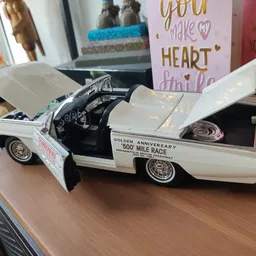 Wit modelauto'tje van een klassieke Amerikaanse auto met openstaande deuren op een houten oppervlak