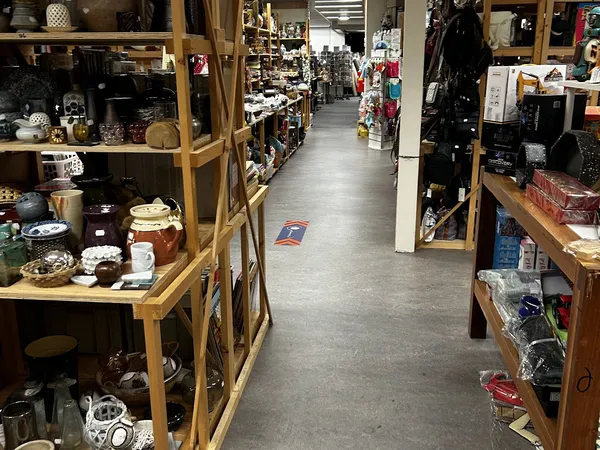 Zicht op de winkelvloer van een kringloopwinkel met houten stellingen vol diverse spullen aan beide zijden