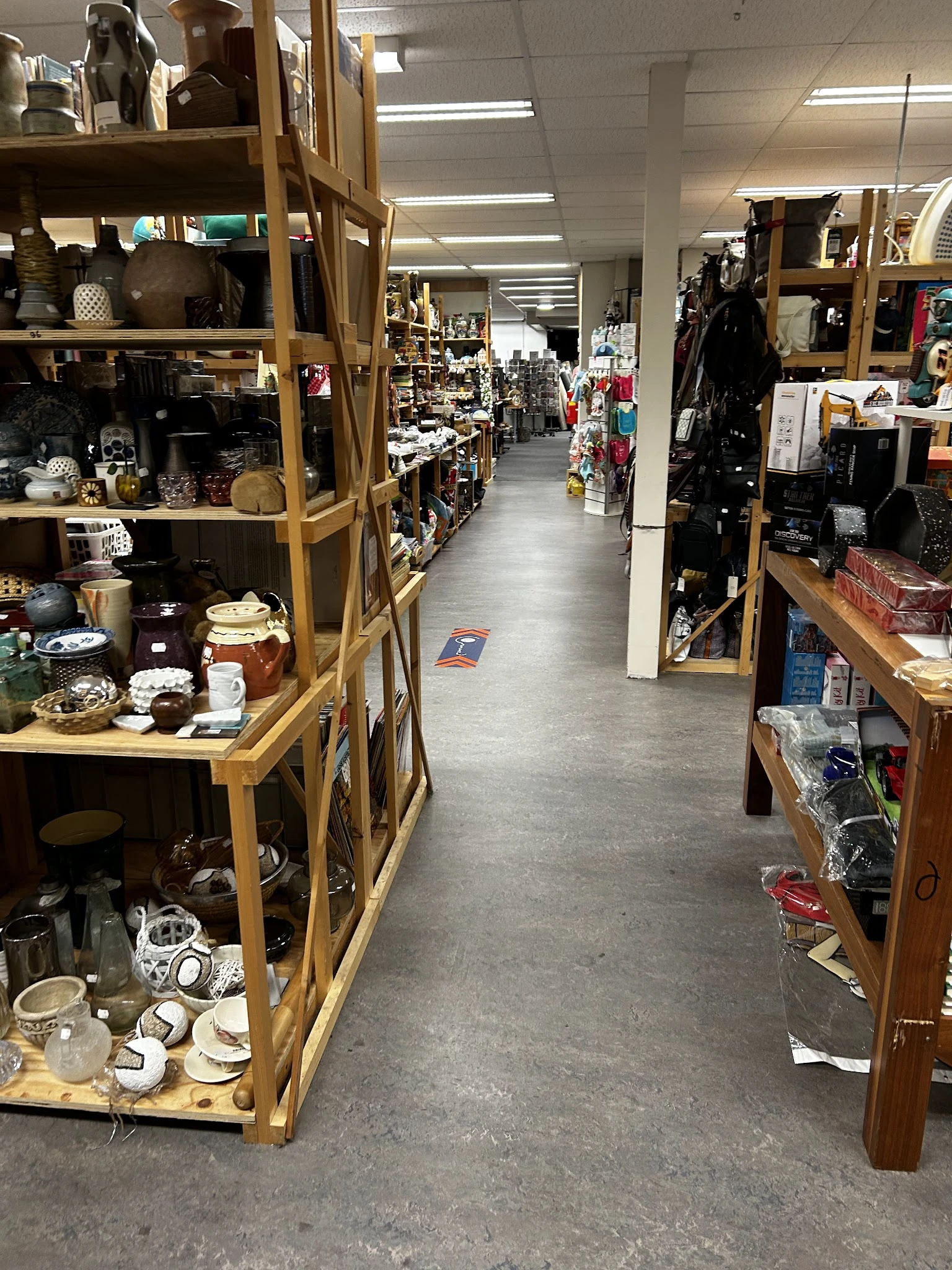 Zicht op de winkelvloer van een kringloopwinkel met houten stellingen vol diverse spullen aan beide zijden