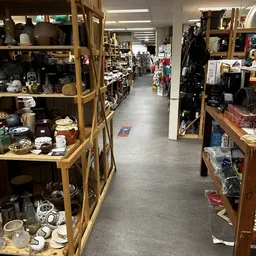 Zicht op de winkelvloer van een kringloopwinkel met houten stellingen vol diverse spullen aan beide zijden