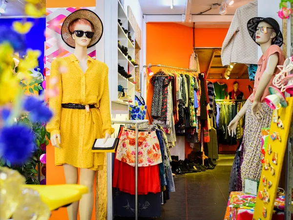 Binnenaanzicht van kringloopwinkel met kleding aan rekken, mannequins in gele jurk en oranje wand, bloemenversiering op voorg
