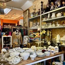 Winkelbinnenruimte met kledingrek links, open stellingen met servies en decoratieartikelen, oranje muur op achtergrond
