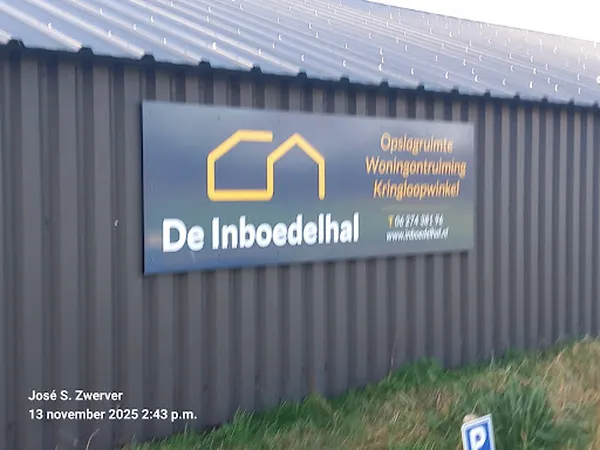 Grijze golfplaten gevel met geel huislogo en witte bedrijfsnaam 'De Inboedelhal'